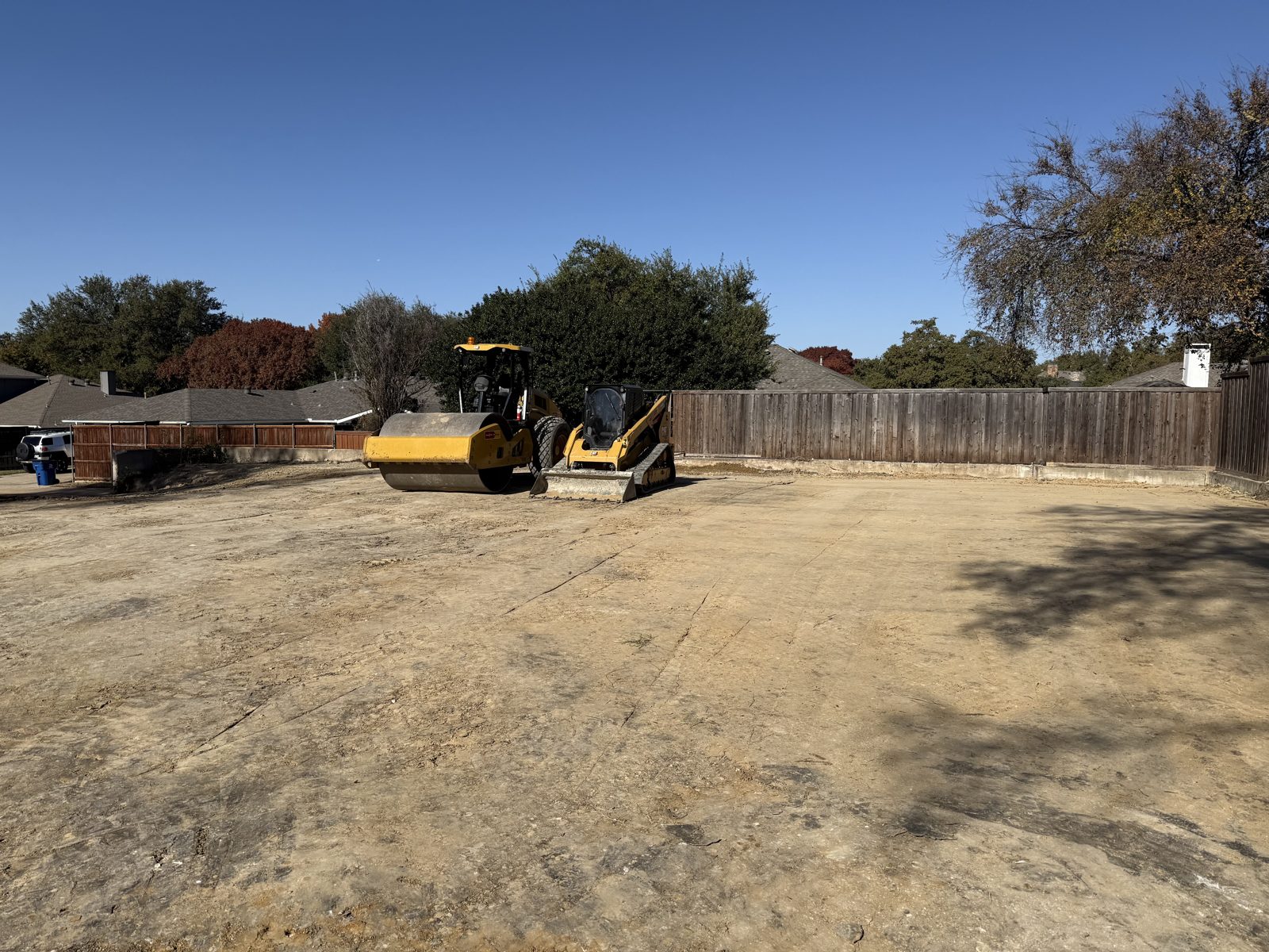 Roller and skid steer compacting a graded house pad on a residential lot